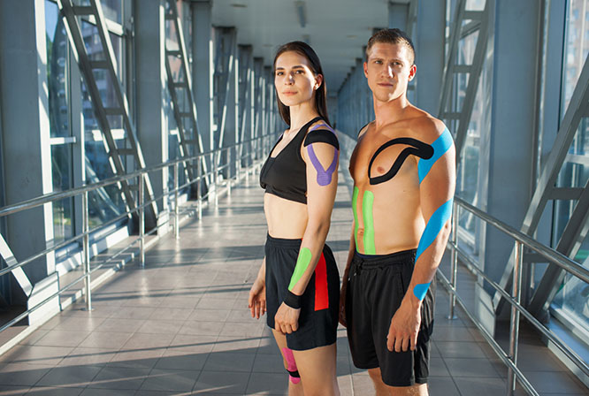 Two athletes are wearing kinesiology tape on their shoulders, arms, and legs to support muscles and help enhance performance during training and exercise